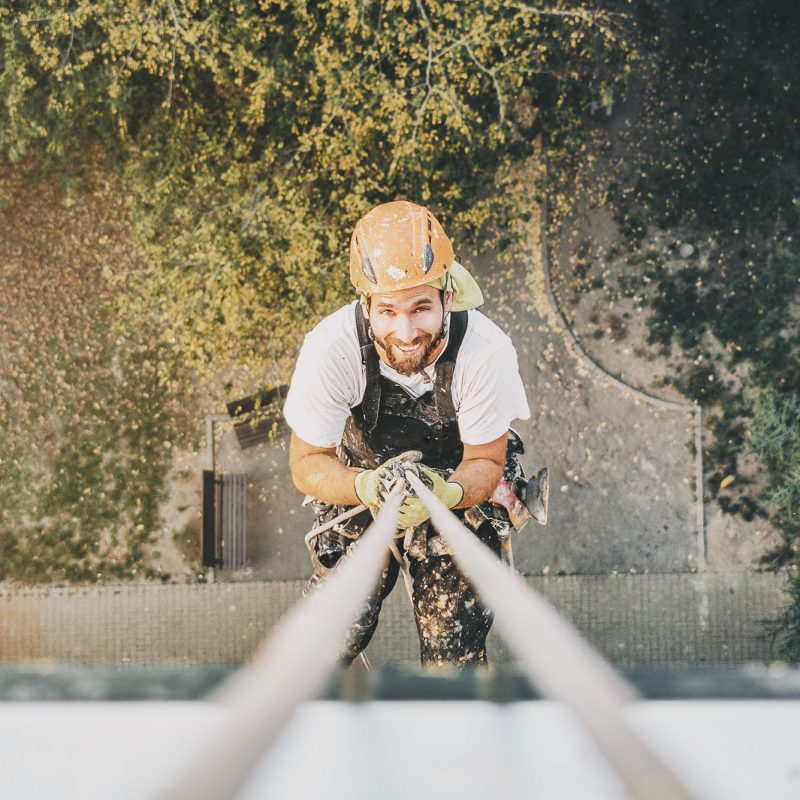 Portrait of Industrial rope access worker hanging from the building while painting the exterior facade wall. Industrial alpinism concept image. Top view. Looking straight to camera